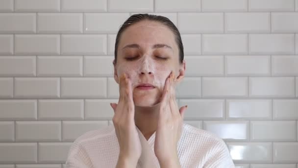 Ung kvinna använder ansiktstvätt skum i badrummet. Kvinna skrubba ansikte med tvål skrubb — Stockvideo