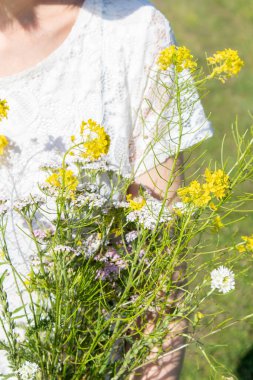 Beautiful Girl with bouquets of wild flowers in a white dress on the meadow.