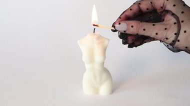 Siyah eldivenli bir kadın kibritle mum yakıyor. Kadın gövdesi şeklinde mum yanıyor.