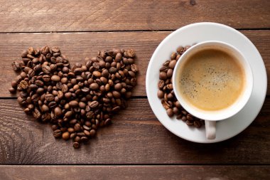 Kalp şeklinde kavrulmuş kahve çekirdekleri ahşap masada bir fincan kahve..