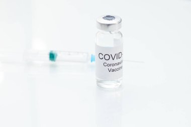 Beyaz cam sehpanın üzerinde Coronavirus aşısı ve şırınga var..
