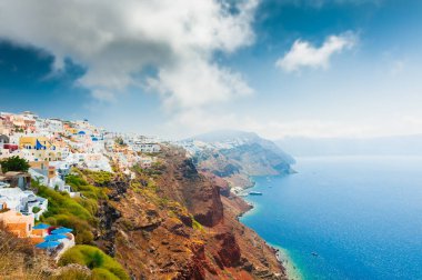 Yunanistan 'ın Santorini adasındaki panoramik manzara. Yaz manzarası, deniz manzarası. Adanın üzerinde bulutlar olan mavi gökyüzü. Meşhur seyahat yeri