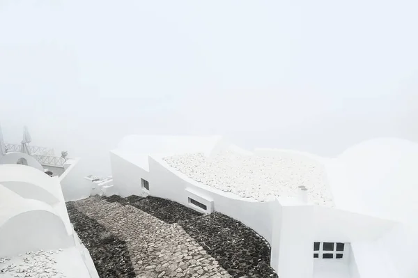 White architecture on Santorini island, Greece. Misty morning with heavy fog. White roofs of the houses and stairs down to the sea