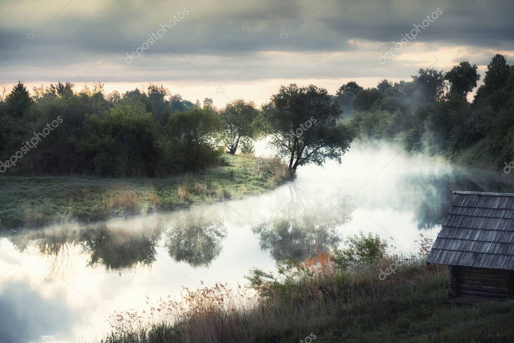 Beautiful summer landscape at misty sunrise. Trees with morning fog are reflected in the river. Suzdal, Russia. 