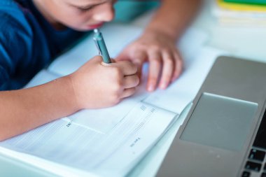 Evde dizüstü bilgisayarı ve sanal bir sınıfta ders çalışan küçük bir okul çocuğunun yakın çekimi. Karantina sırasında uzaktan eğitim ve öğrenme, e-öğrenme, çevrimiçi öğrenme kavramı