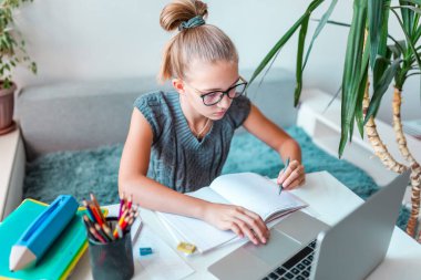 Güzel, genç bir kız solak, evinde bilgisayar ve ders notlarıyla sanal sınıfta çalışıyor. Karantina sırasındaki uzaklık ve çevrimiçi eğitim, e-öğrenme