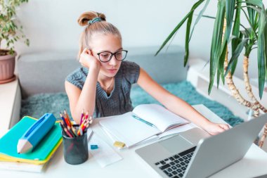 Evde solak, yorgun ve sıkılmış genç bir kız öğrenci evinde bilgisayar ve sanal sınıfta ders çalışan sınıf notlarıyla çalışıyor. Karantina sırasındaki uzaklık ve çevrimiçi eğitim, e-öğrenme