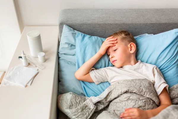高熱と頭痛の床に寝そべっている病気の小さな男の子は額をチェックします コロナウイルスの流行時に家にいて病気になったら — ストック写真