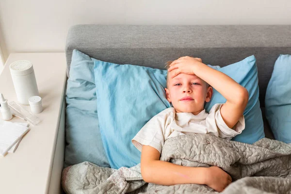 高熱と頭痛の床に寝そべっている病気の小さな男の子は額をチェックします コロナウイルスの流行時に家にいて病気になったら — ストック写真