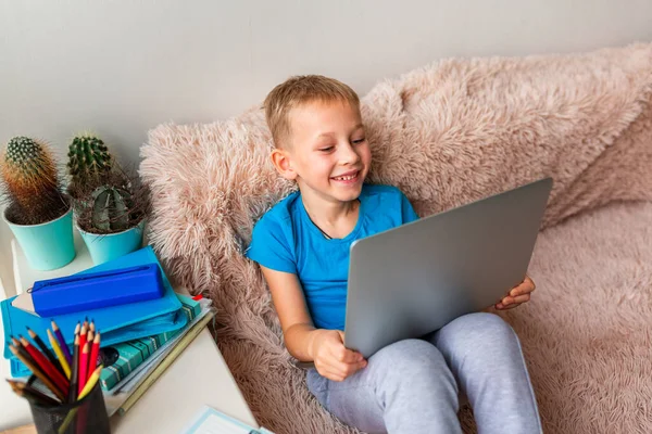 Little young school boy working at home with a laptop and class notes studying in a virtual class. Distance education and learning, e-learning, online learning concept during quarantine