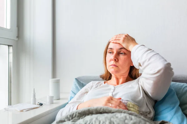 頭痛や熱のある病気の女性は毛布の下に横たわっている コロナウイルスのパンデミックの間 病気の女性はベッドで温度に滞在します 病気の女性は毛布で覆われて高い熱とインフルエンザでベッドに横たわっ — ストック写真