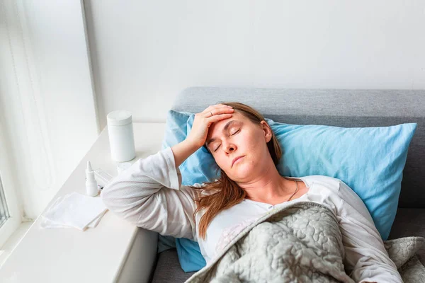 頭痛や熱のある病気の女性は毛布の下に横たわっている コロナウイルスのパンデミックの間 病気の女性はベッドで温度に滞在します 病気の女性は毛布で覆われて高い熱とインフルエンザでベッドに横たわっ — ストック写真