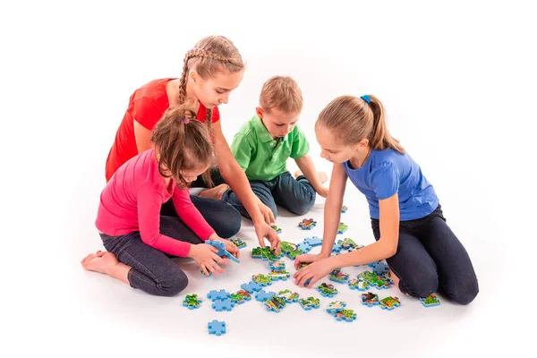 さまざまな年齢の子供たちが一緒にジグソーパズルを解決しました チームワーク 問題概念の解決 — ストック写真
