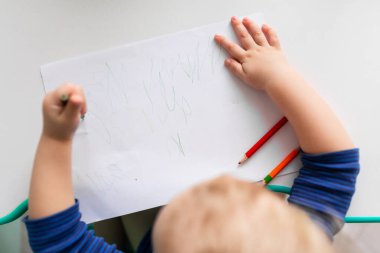 Left handed baby boy drawing a picture with colored pencils clipart