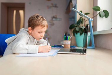 Evde ödevlerini yapan sevimli bir okul çocuğu. Eğitim kitapları ve defter masanın üstünde. Uzaklık öğrenimi çevrimiçi eğitim
