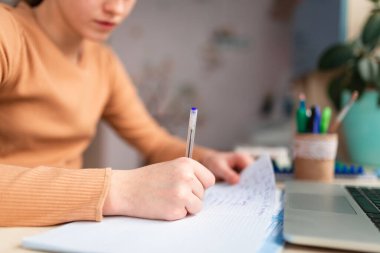 Güzel liseli kız evde ders çalışıyor. Ödev yapıyor. Elim yakın plan. Eğitim kitapları ve defter masanın üstünde. Uzaklık öğrenimi çevrimiçi eğitim