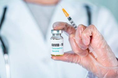 Üniformalı kadın doktor ya da hemşire ve eldivenli yüz maskesi takan laboratuarda koruyucu ilaç şişesinde COVID-19 Coronovirus aşı etiketi taşıyor.