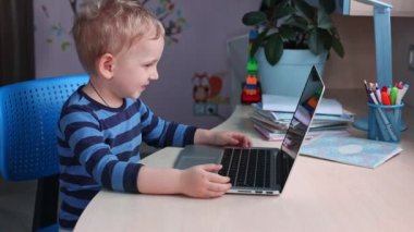 Evde dizüstü bilgisayarda oynayan, kanepede oturan tatlı bebek. Uzaklık öğrenimi çevrimiçi eğitim