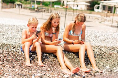 Çocuklar oyun oynuyor ve sahildeki telefonlardan internet arıyor. Deniz kıyısındaki tatilde çocuklar için Gadget bağımlılığı sorunu