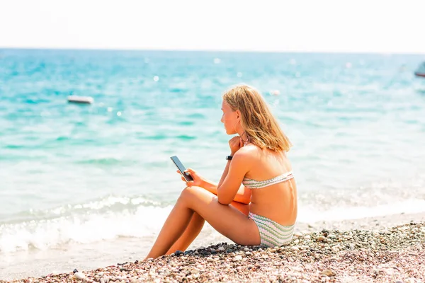 10代の女の子がゲームをプレイし ビーチで電話でウェブを検索します 海辺の概念で休暇中の子供のためのガジェット依存障害の問題 — ストック写真
