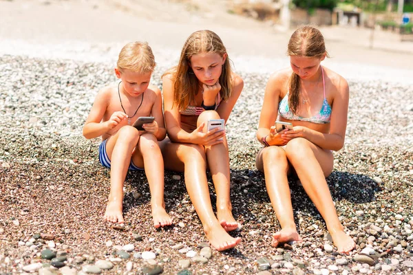 孩子们在海滩上玩游戏和上网搜寻 海滨度假期间儿童小武器依赖障碍问题 — 图库照片