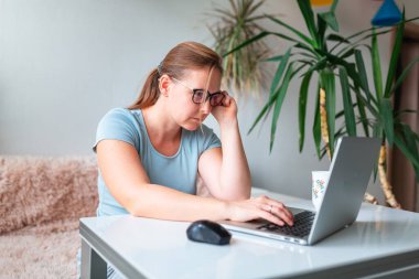 Orta yaşlı bir kadın evdeki masada bilgisayar laptopu kullanarak çalışıyor. Evde çalış ve koronovirüs salgını sırasında evde kal.
