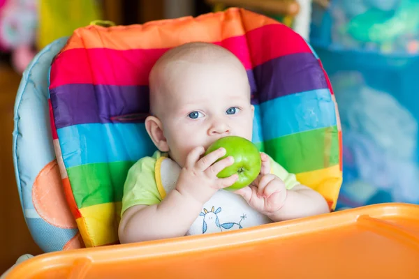 Adorable baby eating apple in high chair — Stock Photo, Image