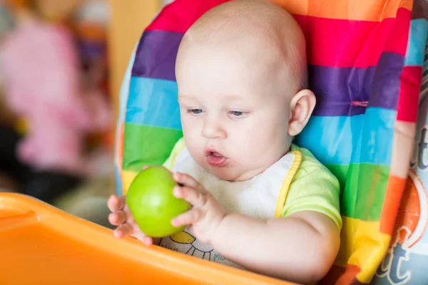 Adorable bebé comiendo manzana en silla alta — Foto de Stock