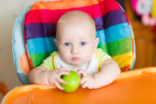 Adorable baby eating apple in high chair — Stock Photo, Image