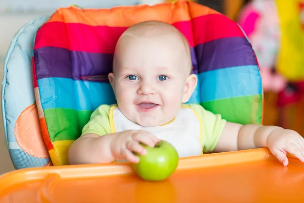 Schattige baby eten apple in hoge stoel — Stockfoto