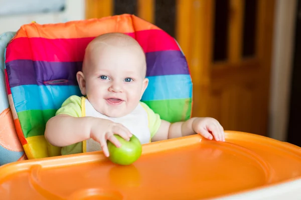 Adorável bebê comendo maçã em cadeira alta — Fotografia de Stock
