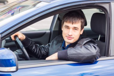 Yakışıklı genç adam arabasında oturuyor.