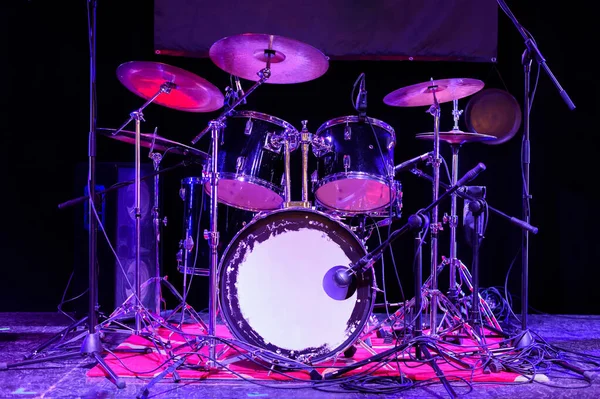 The drum set on the stage. The drum kit is in a dark space and is illuminated by neon light.