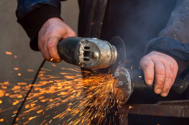 Öğütücü testereyle çalışan adam, aletin görüntüsünü kapat. Elektrikli testere ve kıvılcımlı işçi elleri. Öğütücüyle metal kesen bir işçi