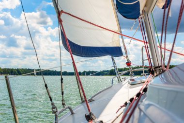 Gölde yelkenli. Ana yelken rüzgarda gerildi, arka planda parlak güneş vardı. Mavi gökyüzünde yelken aç. Rüzgarda süzülürken 