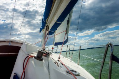 Gölde yelkenli. Ana yelken rüzgarda gerildi, arka planda parlak güneş vardı. Mavi gökyüzünde yelken aç. Rüzgarda süzülürken 