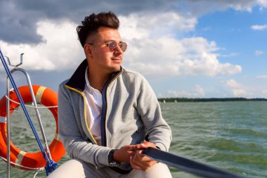 Genç adam yelkenli sürerken güneş banyosu yapıyor. Gölde yaz tatili