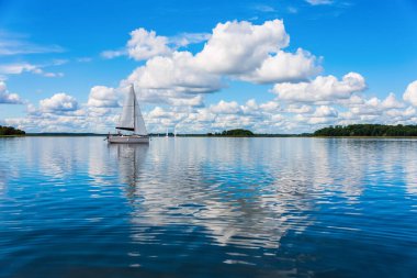 Yağmurdan önce kasvetli gökyüzü ile gölde yelken açmak. Gölde yelken açan bir yat bulutlu mavi bir gökyüzüne karşı. Gölde yelkenli gezisi.