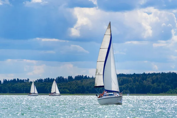 Sailing yacht in the lake with gloomy sky before the rain. Yacht sailing on the lake against a blue sky with clouds. Sailboat vacations on a lake.