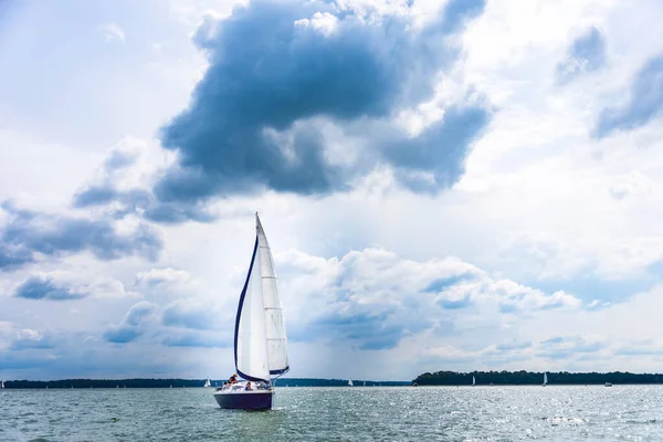 Sailing yacht in the lake with gloomy sky before the rain. Yacht sailing on the lake against a blue sky with clouds. Sailboat vacations on a lake.