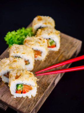 Katsuobushi Uramaki Sushi Roll with salmon and cucumber on wooden board on black background. Sushi roll with dry fish bonito flakes