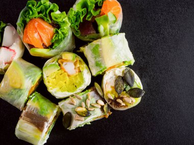 rice paper rolls with salmon, lettuce, shrimp, cucumber, avocado and cream cheese philadelphia on black background. Spring rolls
