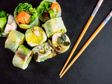 rice paper rolls with salmon, lettuce, shrimp, cucumber, avocado and cream cheese philadelphia on black background. Spring rolls