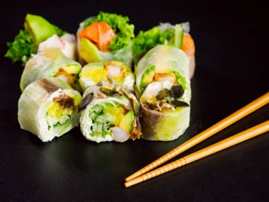 rice paper rolls with salmon, lettuce, shrimp, cucumber, avocado and cream cheese philadelphia on black background. Spring rolls