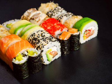 Sushi set, close up view. Various sushi roll with salmon, avocado, cream cheese philadelphia and tobiko flying fish caviar on black background with red chopsticks