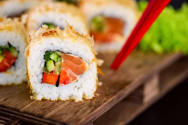 Katsuobushi Uramaki Sushi Roll with salmon and cucumber on wooden board on black background. Sushi roll with dry fish bonito flakes