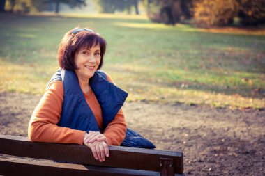 Orta yaşlı beyaz kadın Golden Autumn Park 'ta tek başına oturuyor. Sonbahar manzarasında dinlenen Olgun Kadın