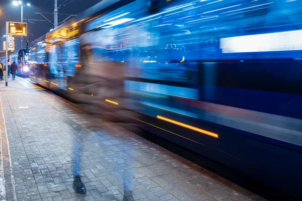 the tram leaves the stop in night city, motion blur view