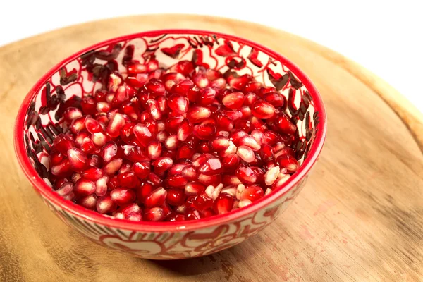 Pomegranate seeds are in a red bowl on the old cutting board — Stock Photo, Image