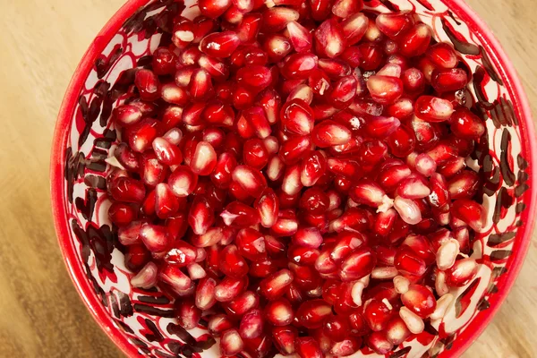 Pomegranate seeds are in a red bowl on the old cutting board — Stock Photo, Image